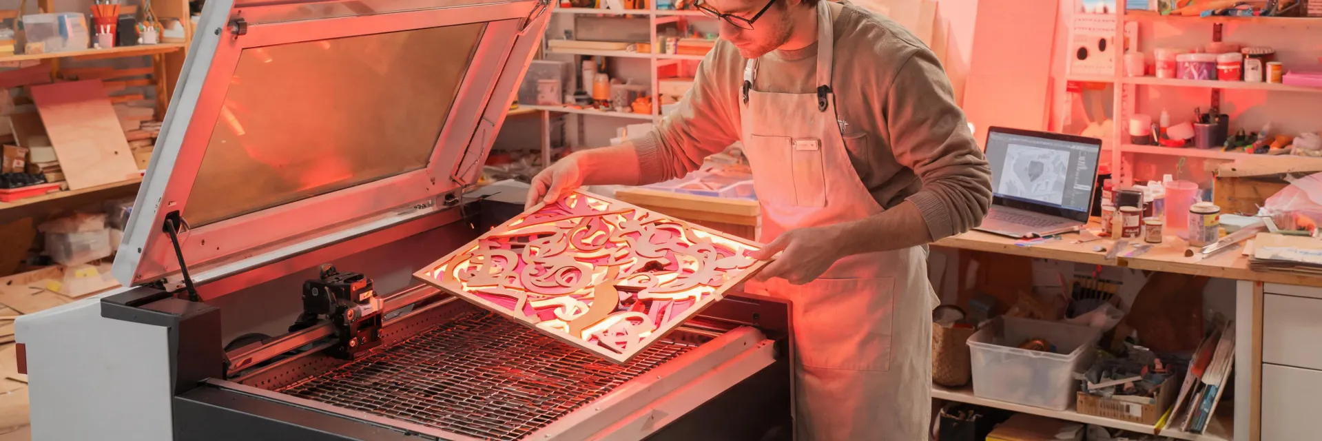 Maker pulling colorful finished artwork off laser bed